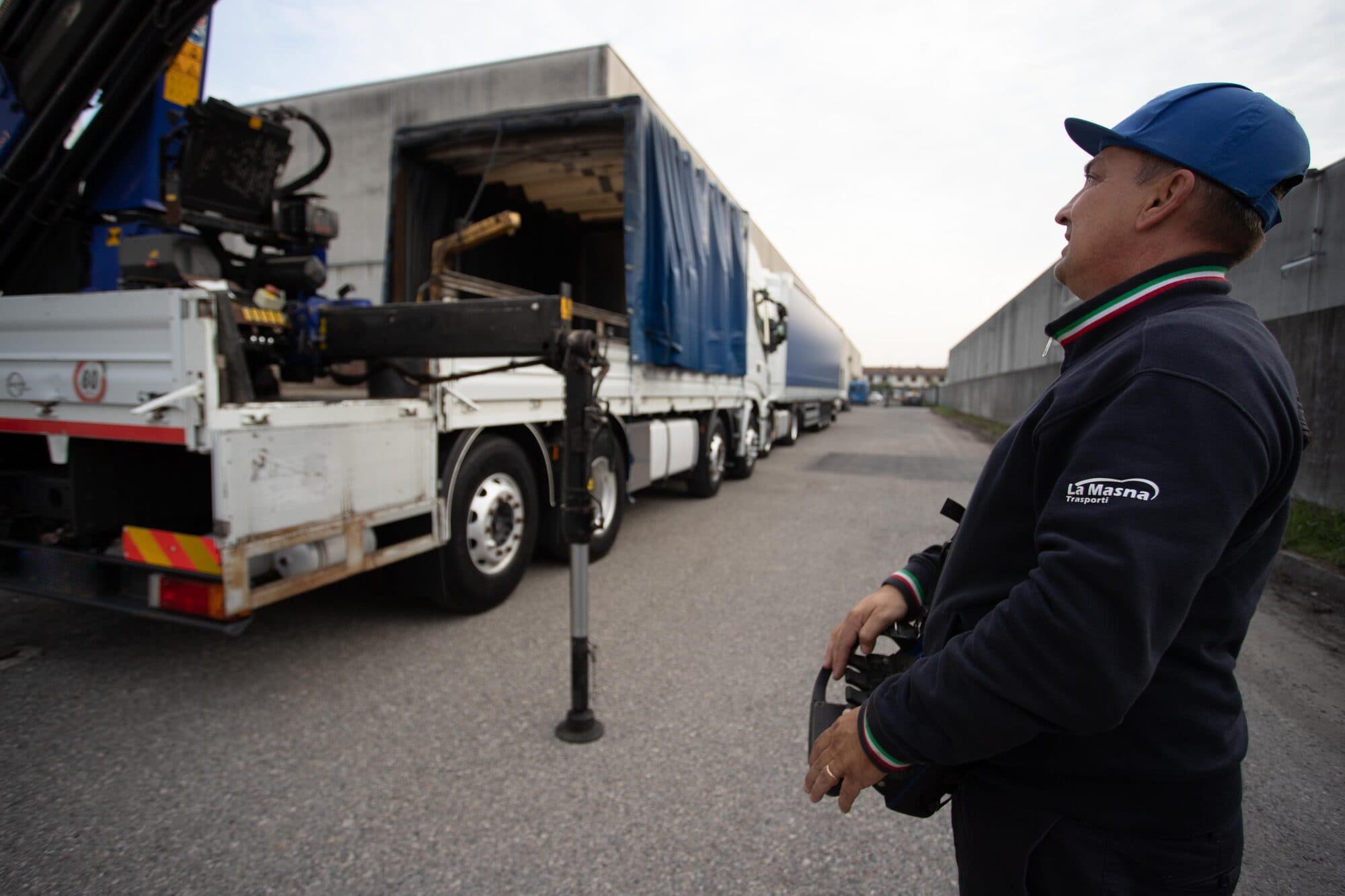 Autista di La Masna Trasporti con il radiocomando in mano segue la manovra della gru, accanto ai mezzi in fila