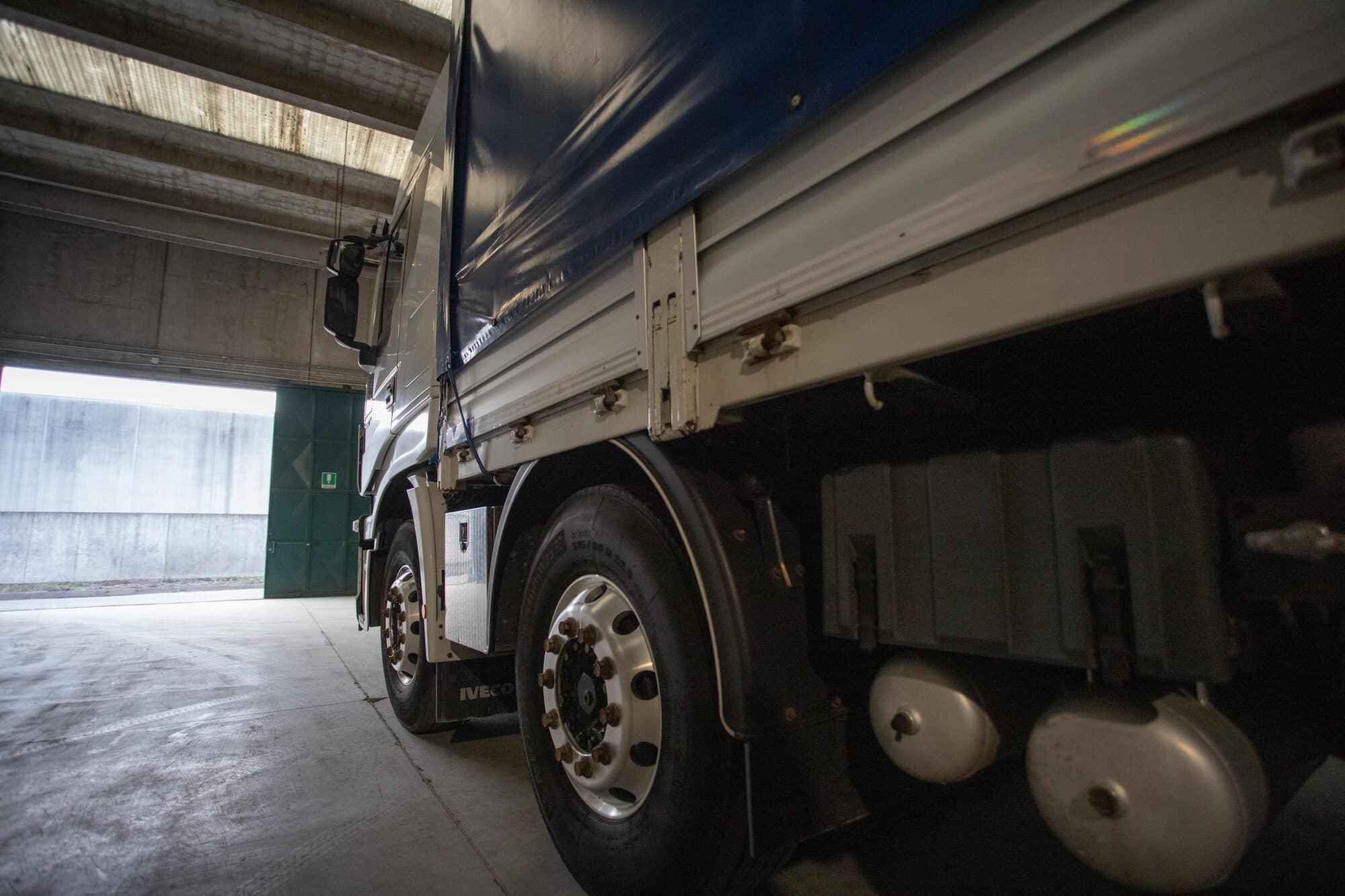 Motrice Iveco cassonata con telone blu nel capannone del deposito, vista dal basso