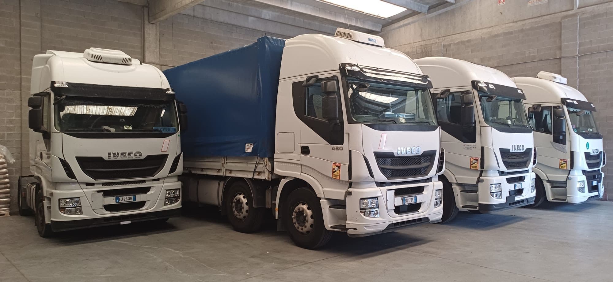 Autoarticolati Iveco Stralis della flotta La Masna fermi nel capannone, con i semirimorchi telonati blu