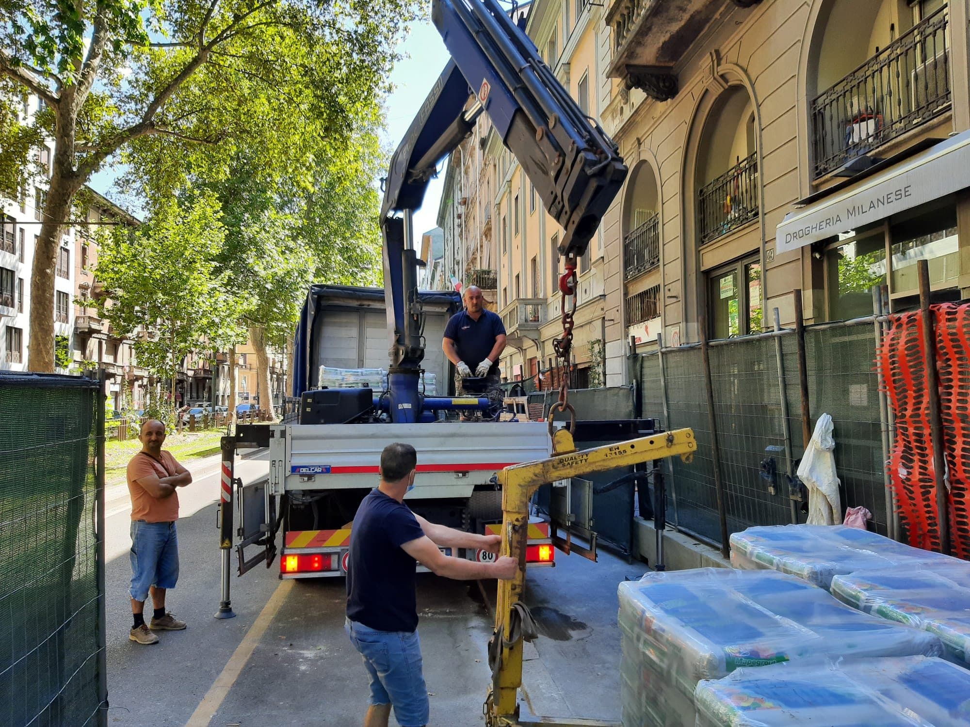 Camion con gru stabilizzato in una via cittadina accanto alla recinzione di un cantiere, con i pallet di materiale appena posati a terra con la forca