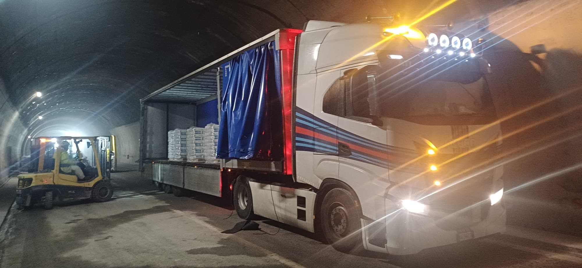 Carico di sacchi pallettizzati con il muletto dal fianco di un semirimorchio telonato con la tenda aperta, di sera