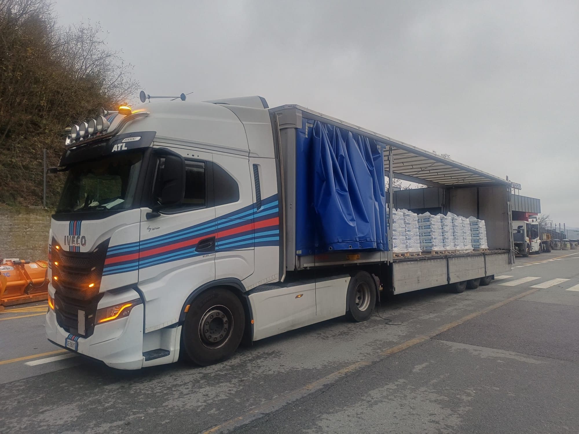 Trattore Iveco con semirimorchio telonato aperto sul fianco e carico di sacchi pallettizzati